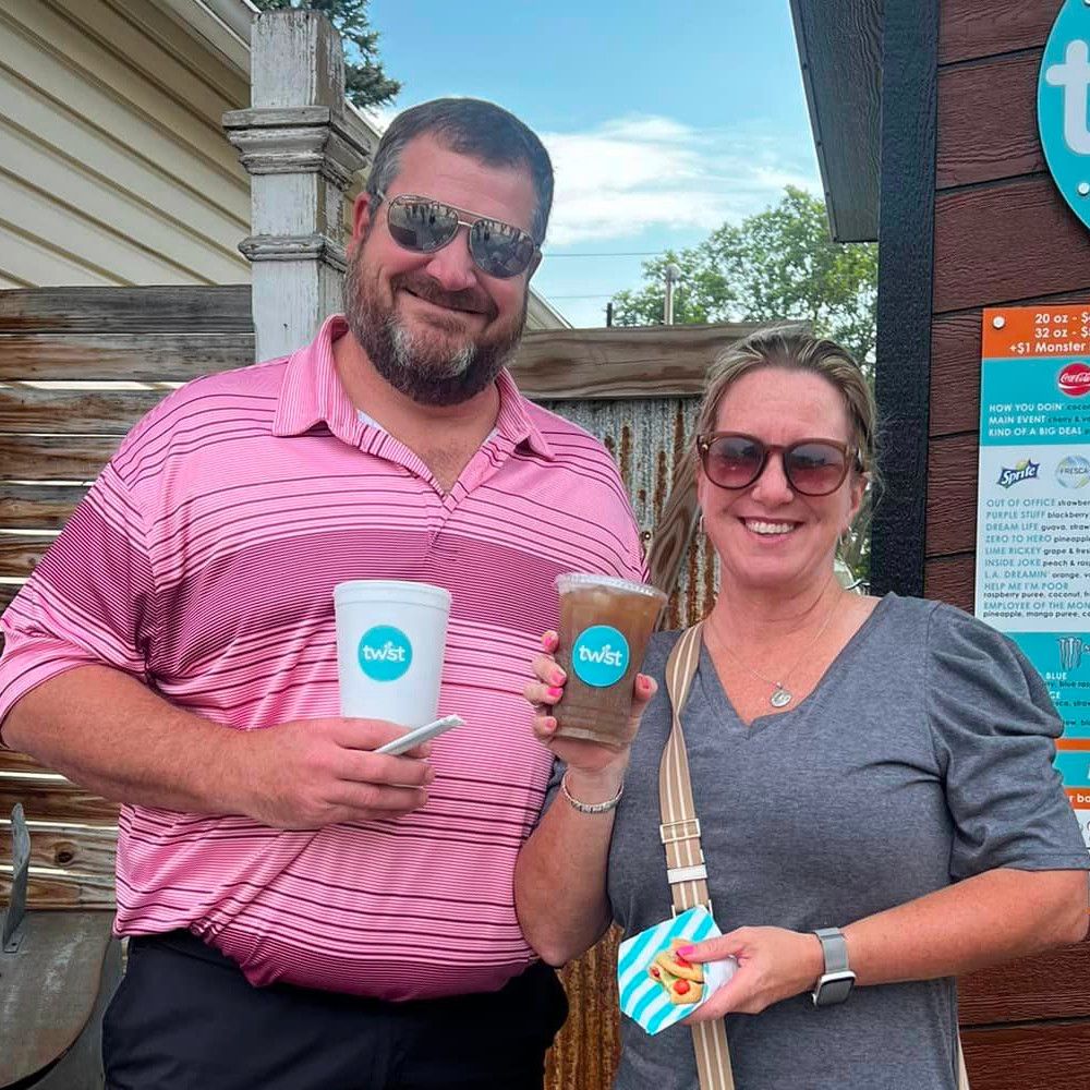 3 smiling people standing in front of Twist's mobile cart, 2 of them holding Twist drinks with gummy worms on top