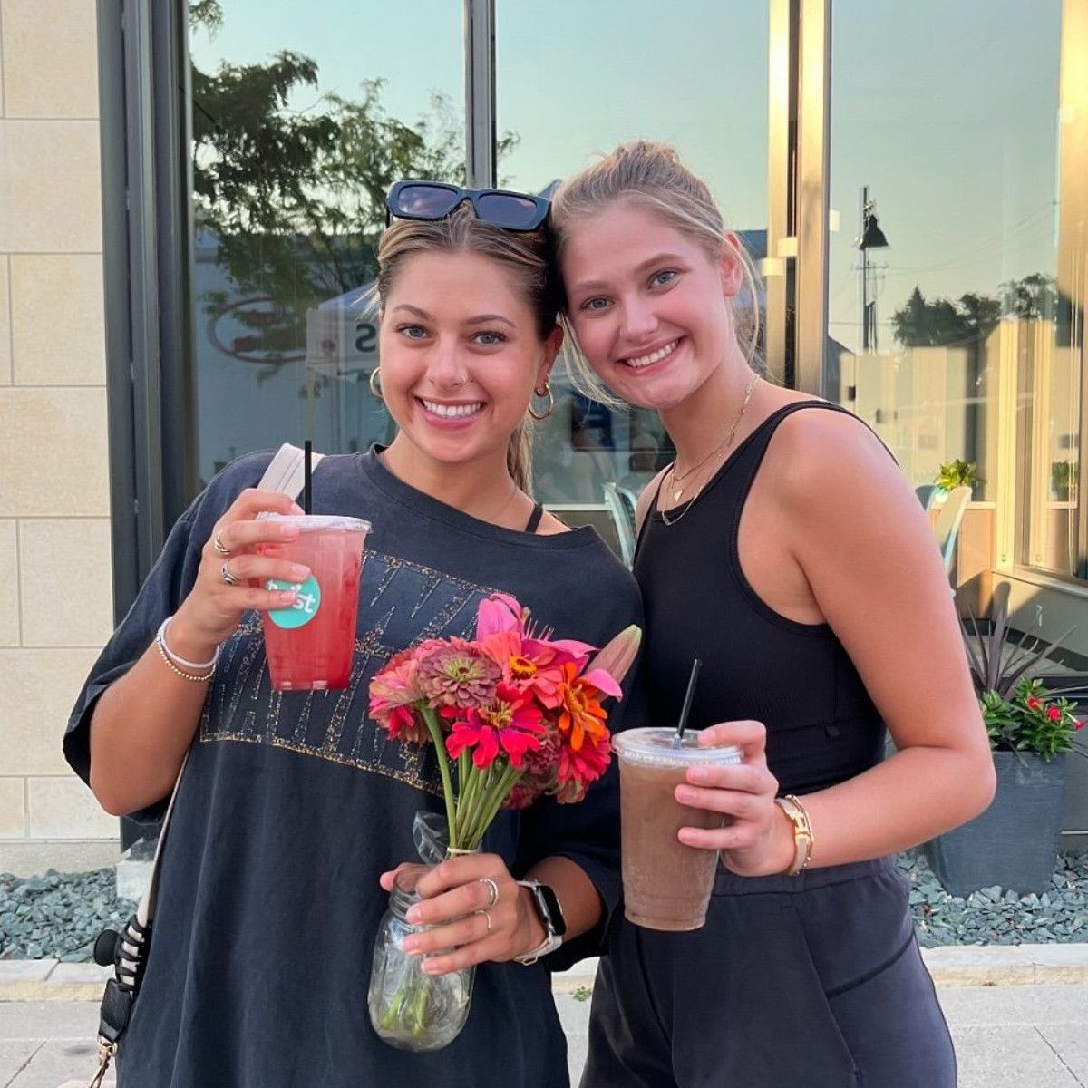 2 people holding their Twist drinks and a vase of red flowers.